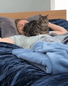 a man laying on a bed with a cat laying on his chest