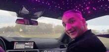 a man sitting in a car with a purple ceiling