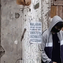 a man in a hooded jacket is standing in front of a wall with a sign on it that says malaban