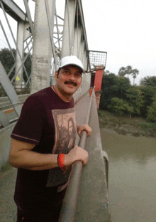 a man wearing a mona lisa t-shirt leans on a railing on a bridge