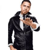 a man wearing a leather jacket and tie is making a stop sign with his hand .