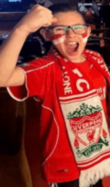 a young boy wearing a scarf and a liverpool shirt is making a thumbs up sign .