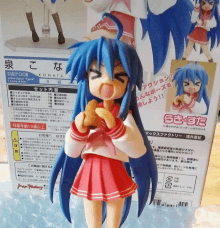 a figurine of a girl with blue hair is standing next to a box that says konata