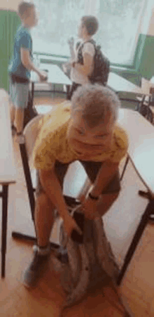 a young boy is sitting on a chair in a classroom with a backpack on his back .