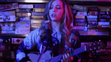 a woman is singing into a microphone while playing a guitar in front of a shelf of board games .