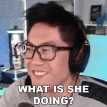 a man wearing headphones and glasses is smiling and asking what is she doing