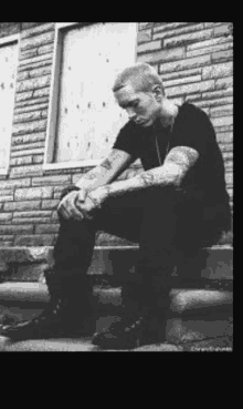 a man with tattoos is sitting on the steps of a building .