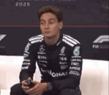 a man in a race car uniform is sitting on a couch holding a phone .
