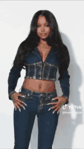 a woman is standing with her hands in her pockets and wearing a denim jacket and jeans .