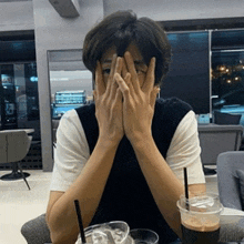 a man covering his face with his hands while sitting at a table with a cup of coffee