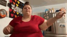 a woman in a red shirt is dancing in a kitchen in front of a sign that says love .