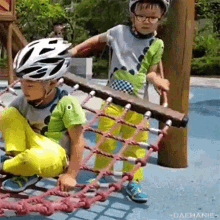 two young boys are playing on a playground . one of the boys is wearing a helmet and glasses .