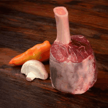 a piece of meat is sitting on top of a wooden table next to vegetables .