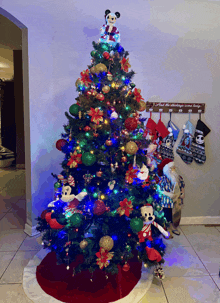 a christmas tree with mickey mouse on top and stockings hanging on the wall behind it