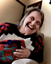 a woman in a christmas sweater is sitting on a couch making a funny face .