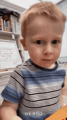 a young boy in a blue and white striped shirt is sitting at a table and making a funny face .