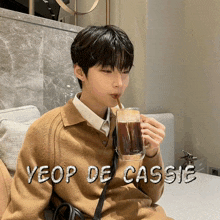 a young man drinking a cup of coffee with the name yeop de cassie written on the bottom