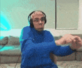 a man wearing headphones and a blue sweater is sitting on a couch .