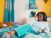 a woman sits on a bed talking on a phone