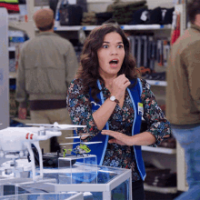 a woman wearing a blue vest with the word super on it stands in front of a display of drones