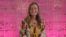 a woman in a yellow top is smiling in front of a pink background with the letter p on it