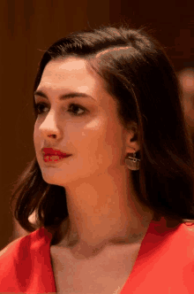 a close up of a woman 's face wearing a red shirt and earrings