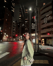 a woman in a green jacket stands in front of a red traffic light