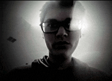 a young man wearing glasses is taking a selfie in a dark room .