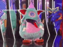 a masked singer character is standing on a stage wearing a pink and green costume .