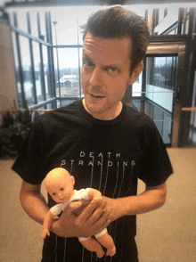 a man wearing a death stranding t-shirt is holding a doll