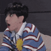 a young man wearing a blue and white striped sweater is sitting on a couch with his mouth open .