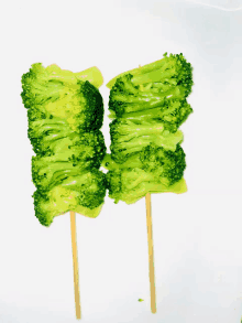 two sticks of broccoli are stacked on top of each other on a white surface