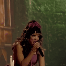a woman dressed as a fairy is singing into a microphone while wearing a flower in her hair .