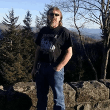 a man wearing a black shirt that says iron riders mc is standing on a rocky hillside .