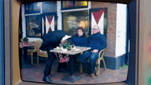 a tv screen shows a couple sitting at a table in front of a store that says ' open your gardens '