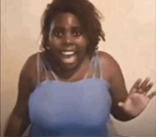 a woman in a blue tank top is making a funny face and waving her hand .