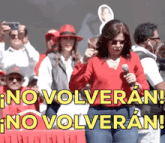 a woman stands in front of a crowd holding a microphone and a sign that says " no volveran "