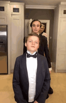 a boy in a tuxedo stands next to another boy