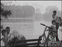 a black and white photo of a group of people sitting on a bench with a bicycle in the foreground .