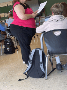 a woman in a pink tank top is standing next to a boy in a classroom