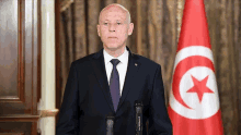 a man in a suit and tie is standing in front of a flag with a red star on it .