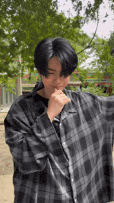a young man wearing a plaid shirt is standing in front of trees