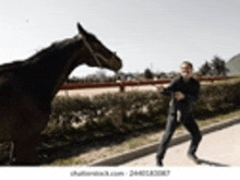 a man is walking next to a large black horse on a sidewalk .