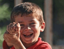 a young boy is pointing at the camera while laughing .