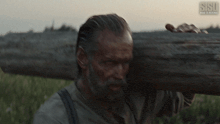 a man is carrying a large log over his shoulder and the letters ssi are visible in the corner