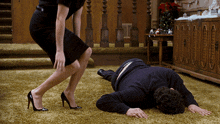 a woman standing next to a man laying on the floor with his head on his knees