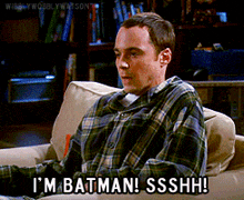 a man in a plaid shirt is sitting on a couch saying i 'm batman ssshh