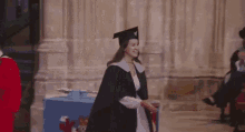 a woman in a graduation cap and gown is standing in front of a blue box with a coat of arms on it .