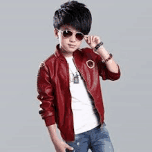 the boy is wearing sunglasses and a red leather jacket .