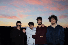 a group of young men posing for a photo with a sunset in the background